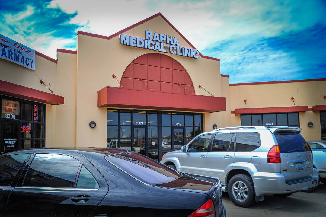 Exterior view of Rapha Medical Clinic storefront with parked vehicles in front under a partly cloudy sky