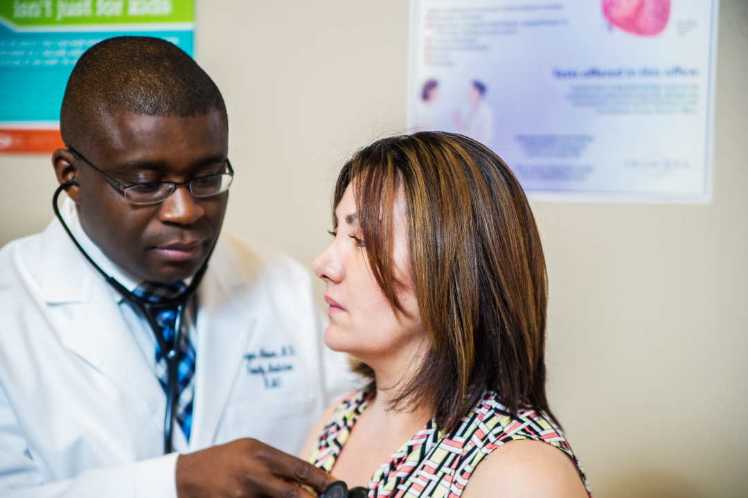 Male family doctor using a stethoscope to examine a female patient's heart and lungs during a routine checkup