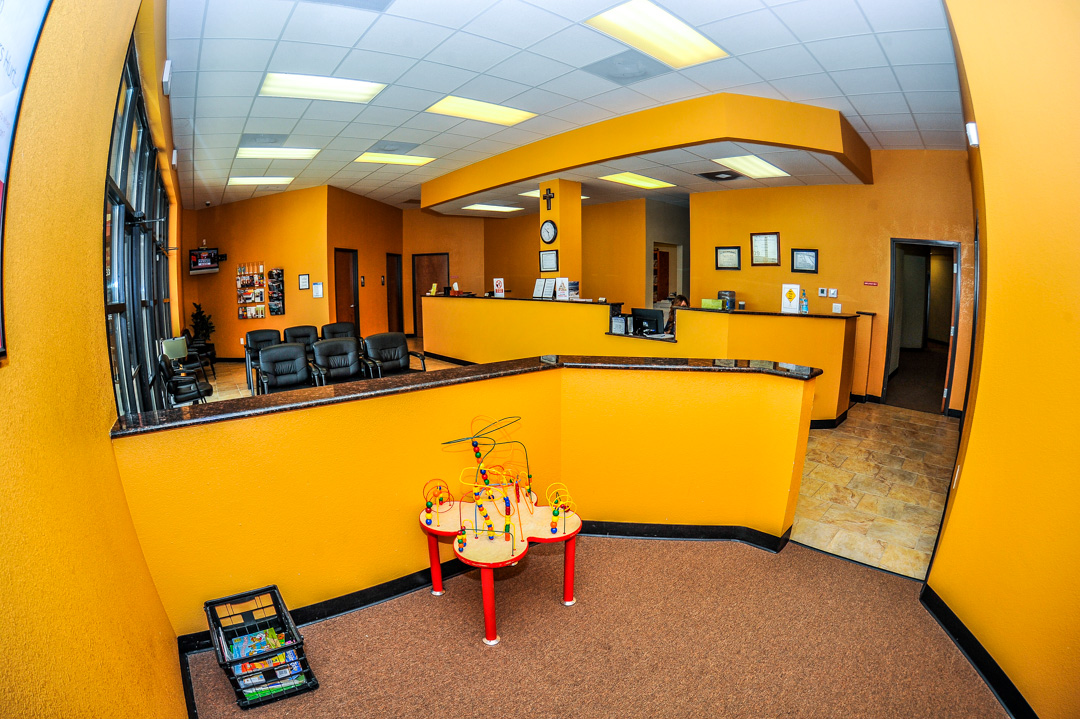 Wide-angle interior view of Rapha Medical Clinic waiting room featuring yellow walls, reception desk, seating area, and a children's activity table